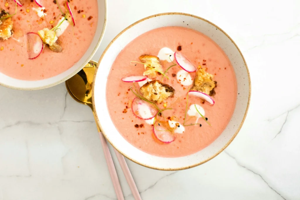Creamy pink soup topped with radish slices, croutons, and herbs