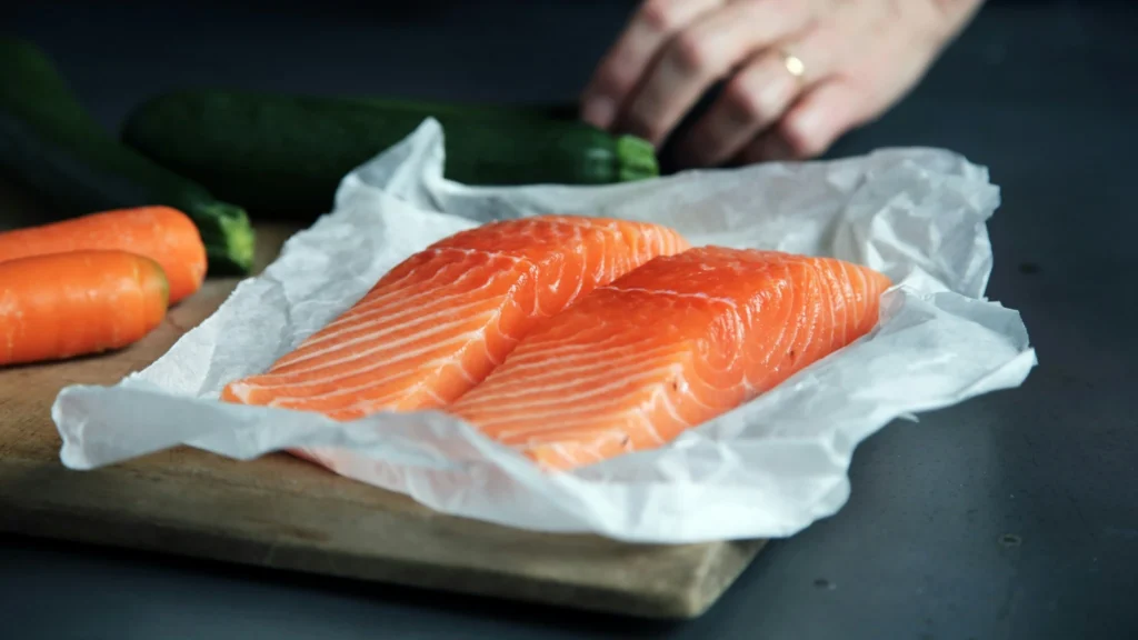 Fresh salmon fillets on parchment paper with carrots and zucchini on a cutting board