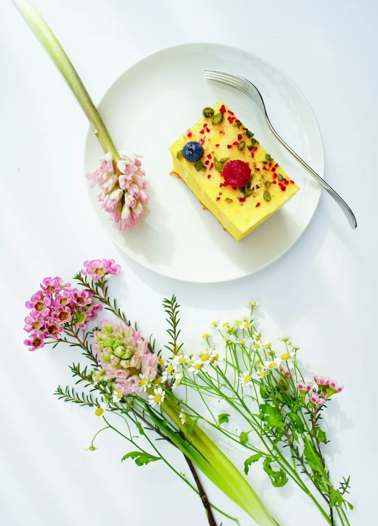 Lemon dessert slice topped with berries and nuts on a white plate