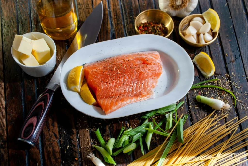 Raw salmon fillet on plate with lemon wedges, garlic, herbs, and olive oil on rustic table