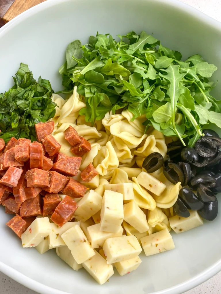 Pepperoni, cheese, olives, basil, and arugula added to cooked tortellini for antipasto salad.
