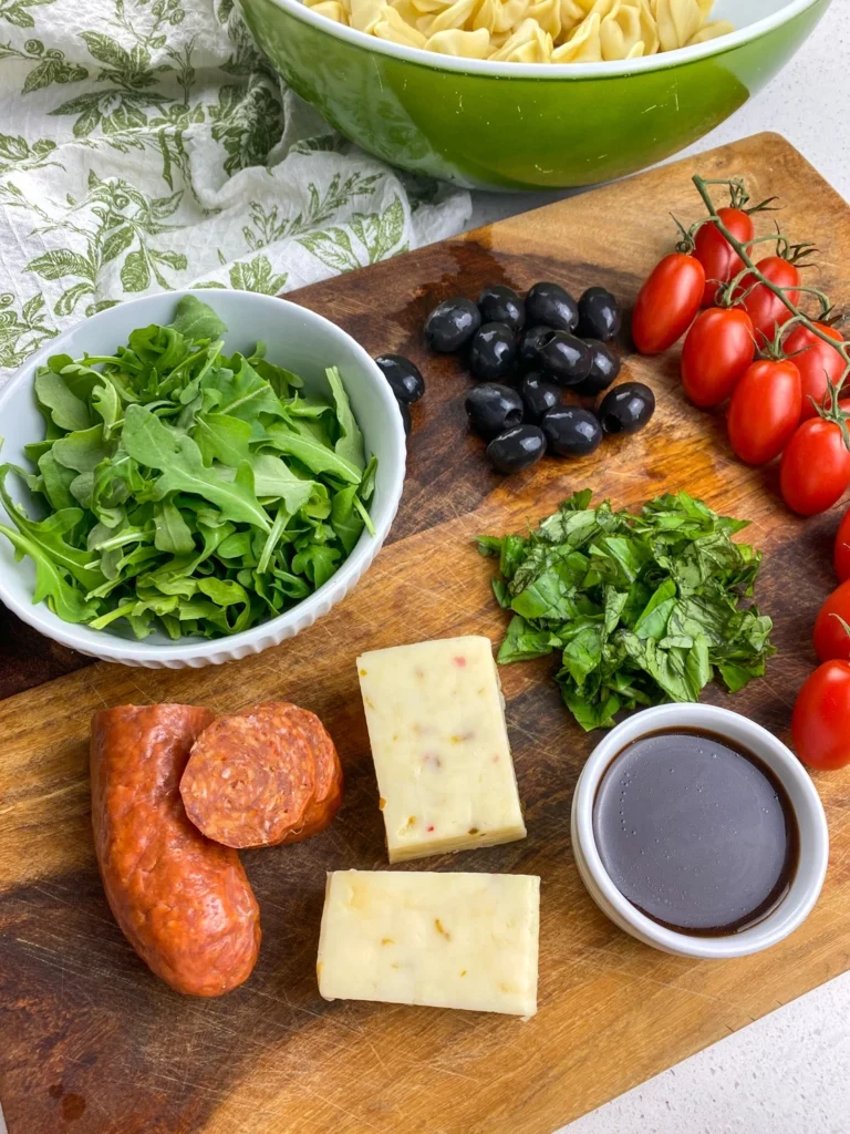 Ingredients for tortellini antipasto salad arranged on a wooden cutting board.