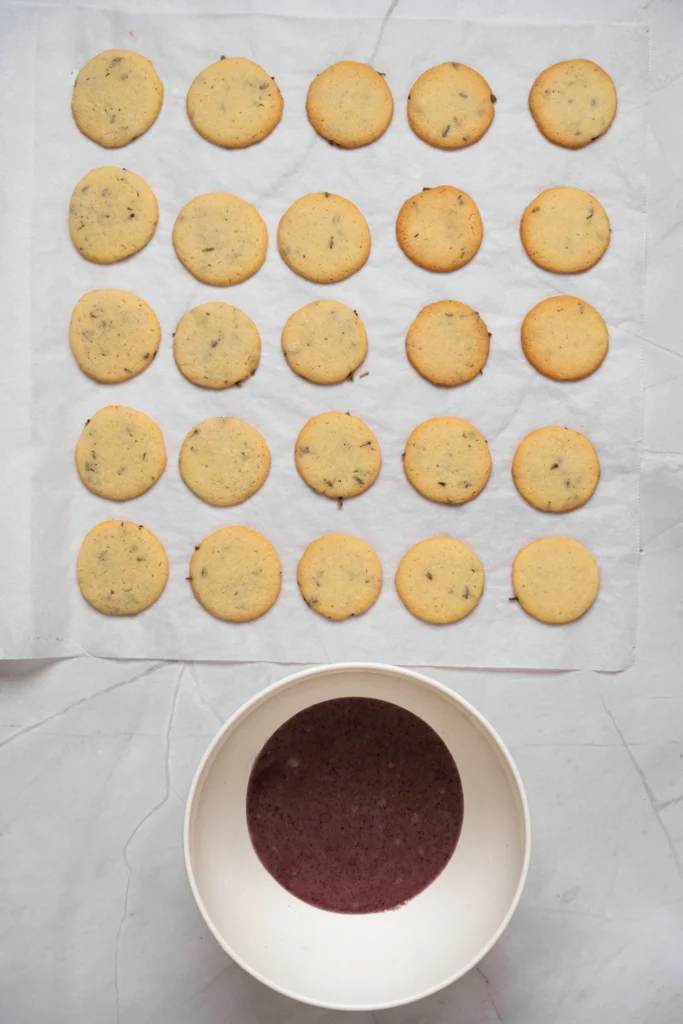 Freshly baked lavender cookies beside a bowl of purple lavender icing.