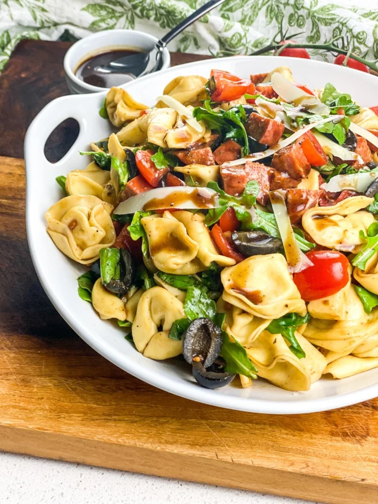 Close-up of tortellini antipasto salad with balsamic vinaigrette, olives, tomatoes, and shaved Parmesan.