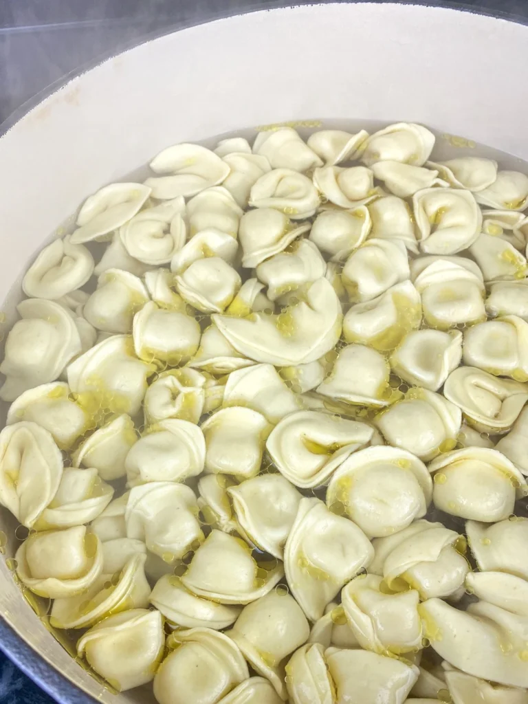Adding olive oil to tortellini while it cooks in boiling water.