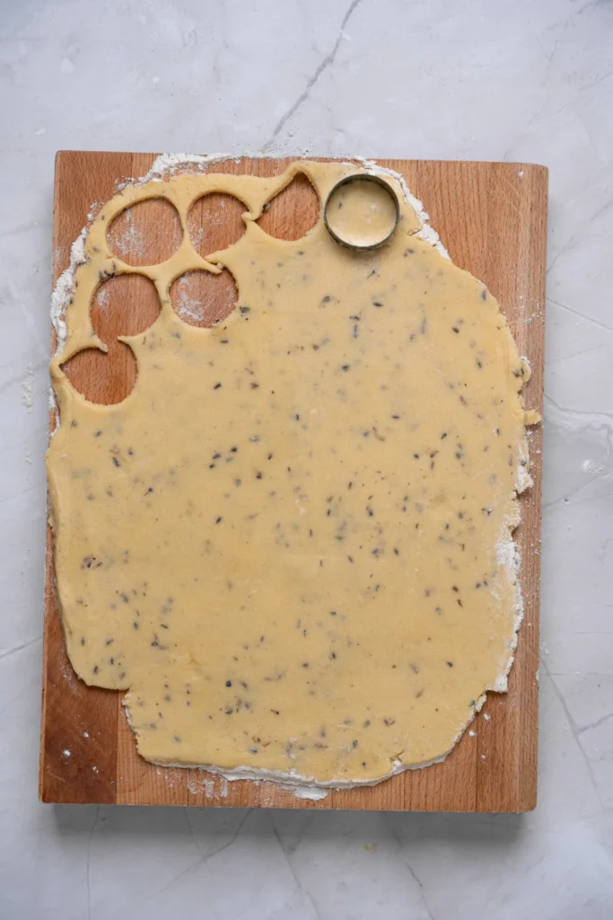 Round cookie cutter cutting lavender cookies from rolled cookie dough.