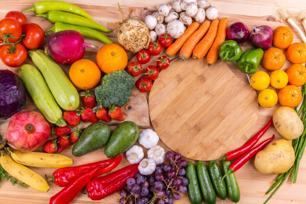 Flatlay of fresh fruits and vegetables arranged around a wooden cutting board.