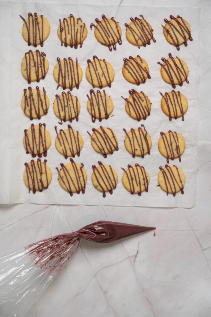 Lavender cookies drizzled with purple icing on parchment paper.