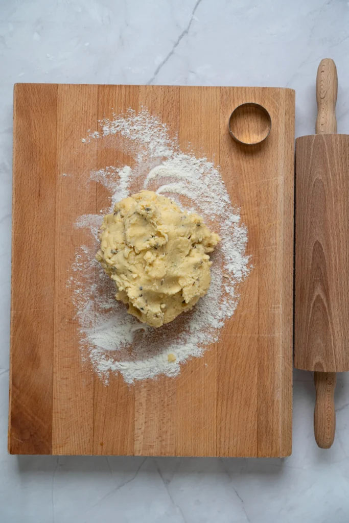 Lavender cookie dough resting on a floured wooden board beside a rolling pin.