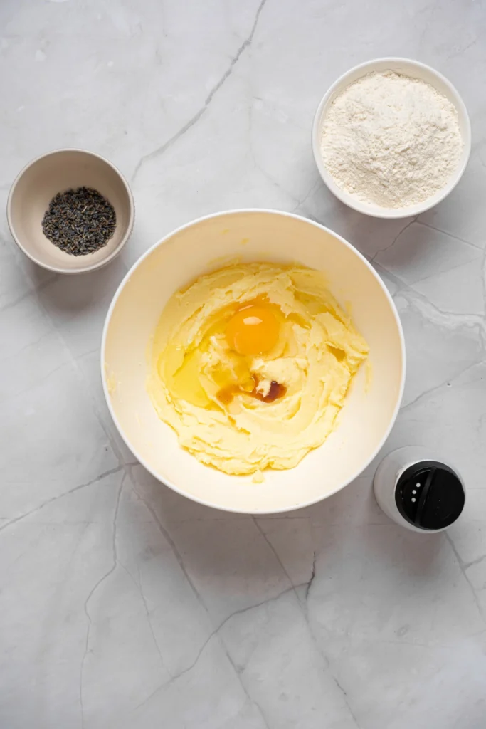 Egg and vanilla extract being added to creamed butter mixture for lavender cookies.