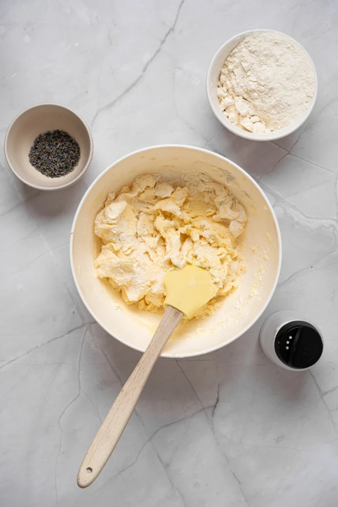 Lavender cookie dough partially mixed with flour in a large mixing bowl.