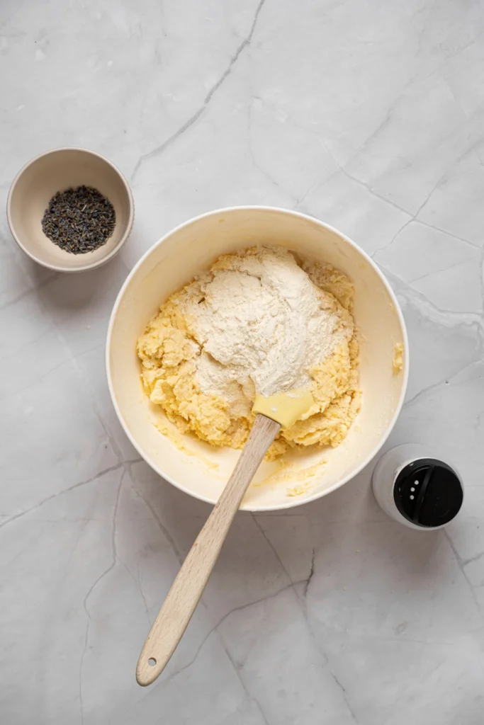 Flour being folded into lavender cookie dough with a spatula.
