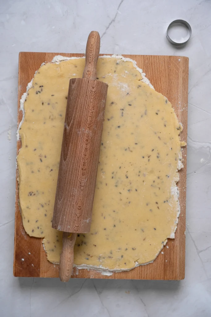 Lavender cookie dough rolled out on a floured wooden board with a rolling pin.