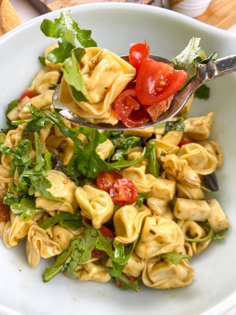 Spoonful of tortellini antipasto salad with tomatoes, arugula, cheese, and pepperoni.