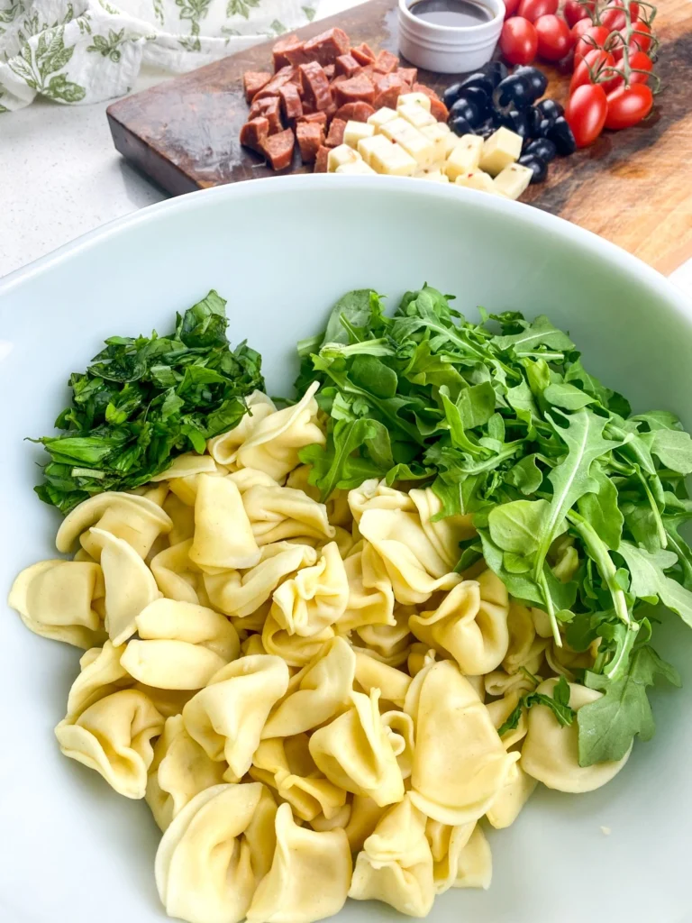 Fresh basil and arugula added to cooked tortellini for antipasto salad.