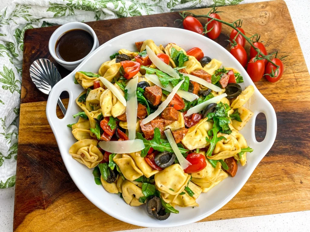 Serving platter filled with tortellini antipasto salad topped with shaved Parmesan cheese.