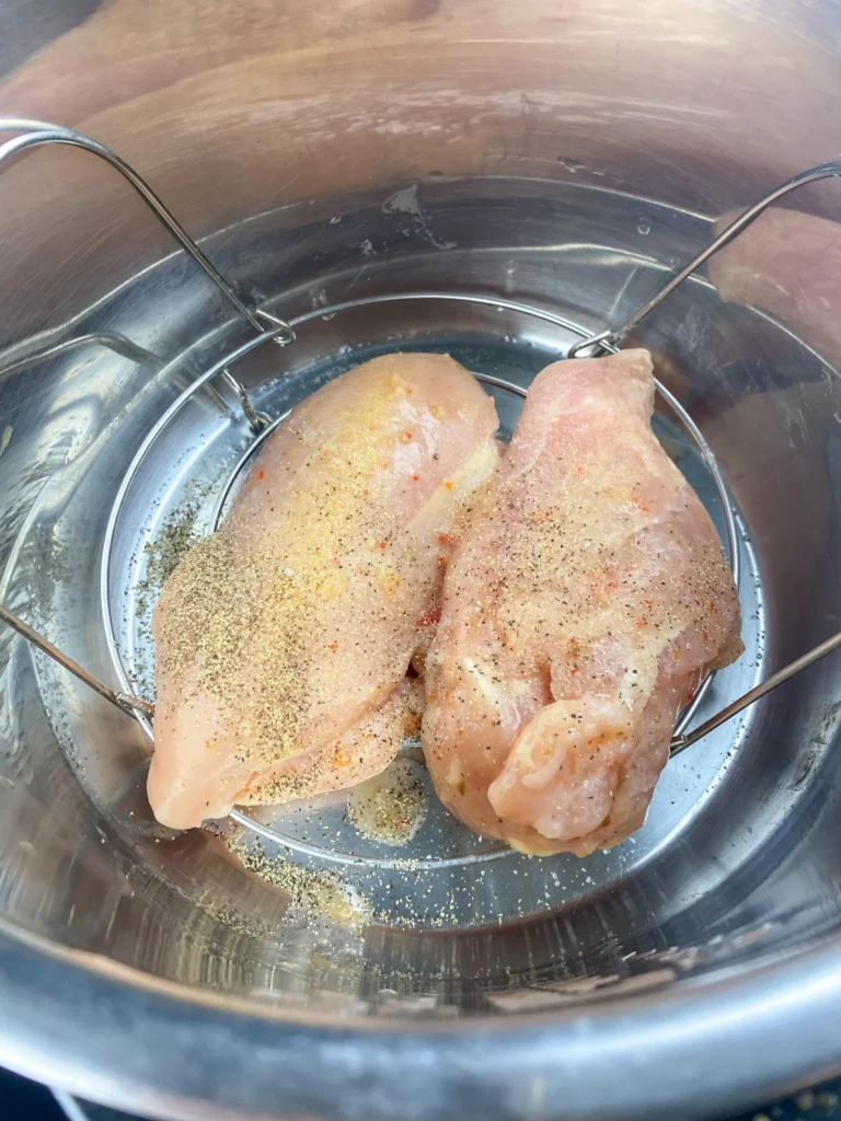 Chicken breasts seasoned with garlic powder, salt, and pepper in an Instant Pot insert.