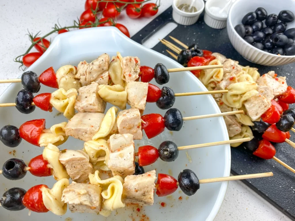 Finished tortellini chicken skewers with olives, tomatoes, and chicken arranged on wooden skewers.