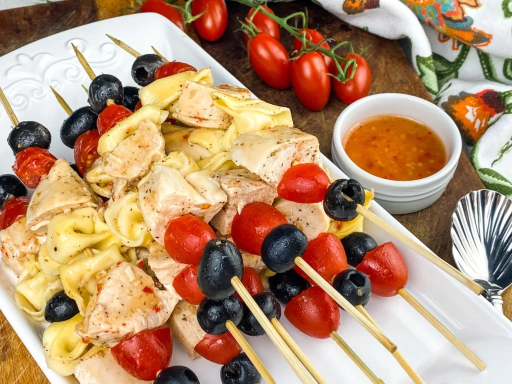 Close-up of tortellini chicken skewers with tomatoes and black olives on a serving tray.