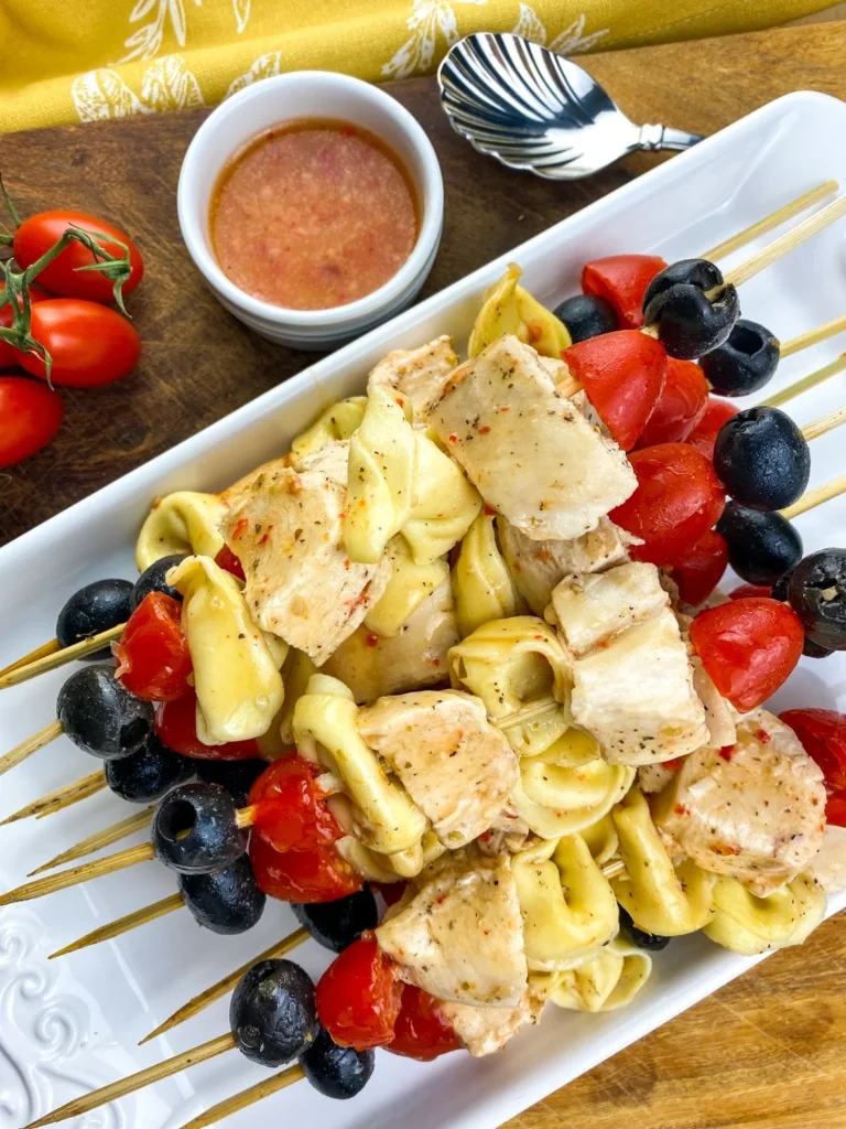 Overhead view of tortellini chicken skewers served on a white platter with dipping sauce.