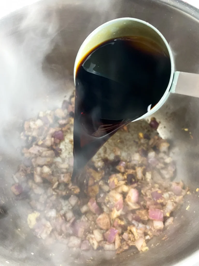 Balsamic vinegar being poured into the Instant Pot to deglaze the onion and spice mixture.