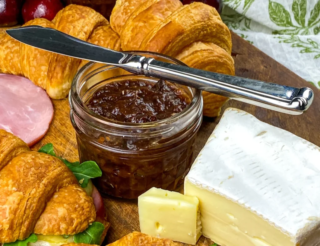 Close-up of homemade Instant Pot cherry chutney spread on a knife with croissants and Brie in the background.