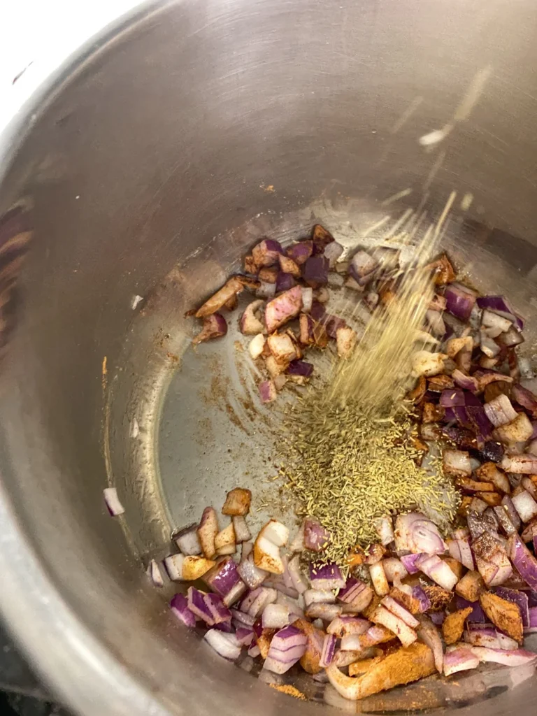Dried rosemary being added to the sautéed onion and spice mixture for Instant Pot cherry chutney.