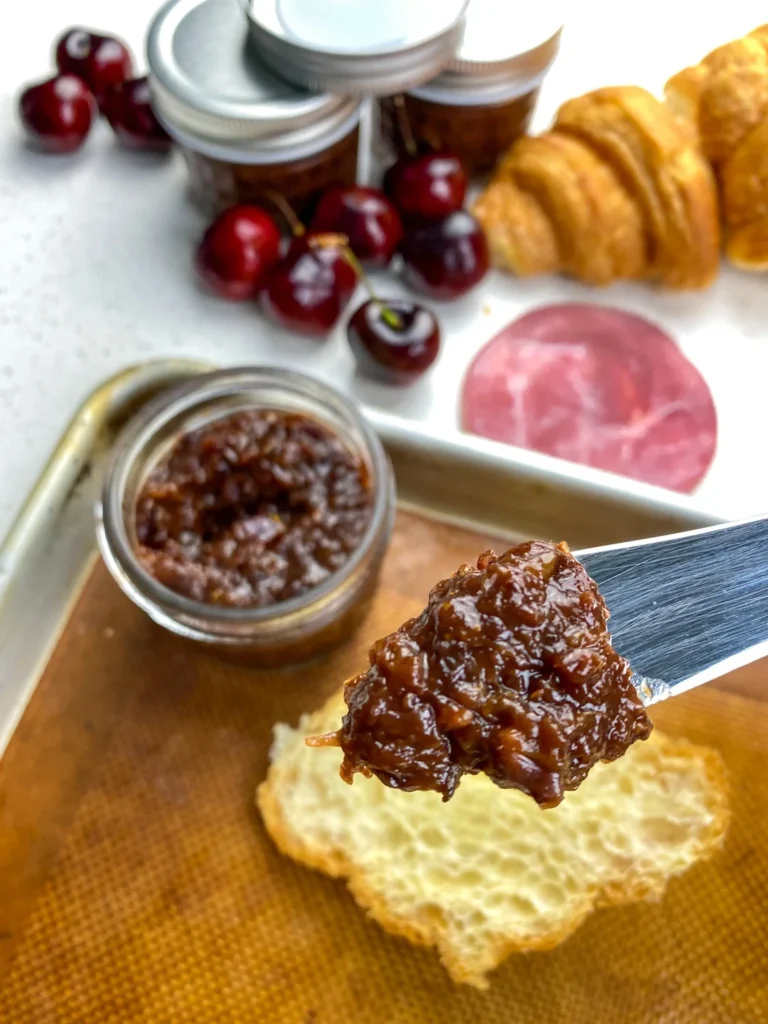 Instant Pot cherry chutney served with Brie cheese, croissants, ham, and fresh cherries on a serving board.
