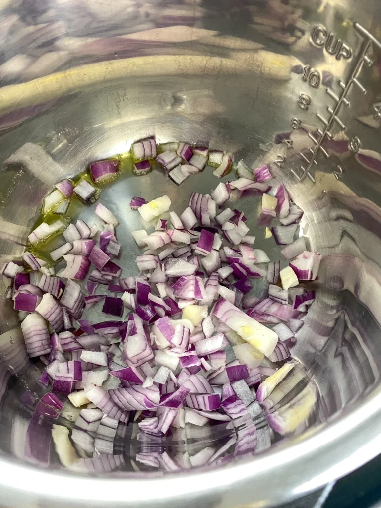 Chopped red onions sautéing in olive oil in an Instant Pot before making cherry chutney.