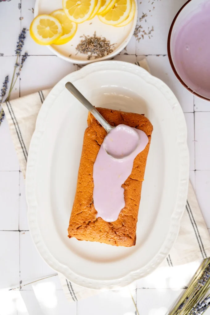 Pale purple lemon lavender glaze being spooned over the top of the cooled pound cake.