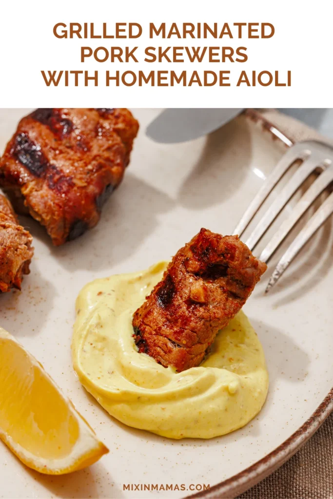 Piece of grilled marinated pork dipped in creamy homemade aioli with lemon on the plate.