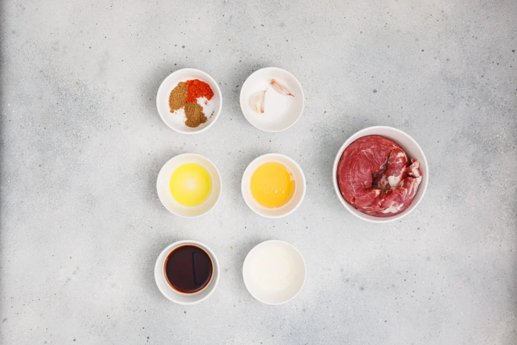 Ingredients for grilled pork skewers with homemade aioli arranged in bowls.
