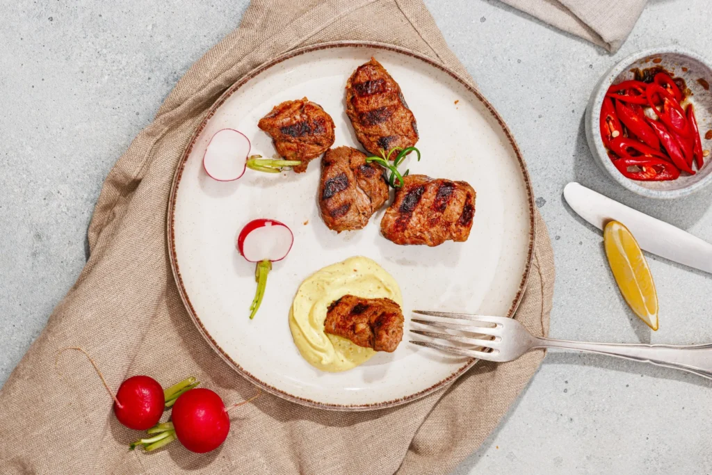 Grilled pork served with homemade aioli, radishes, and a lemon wedge.