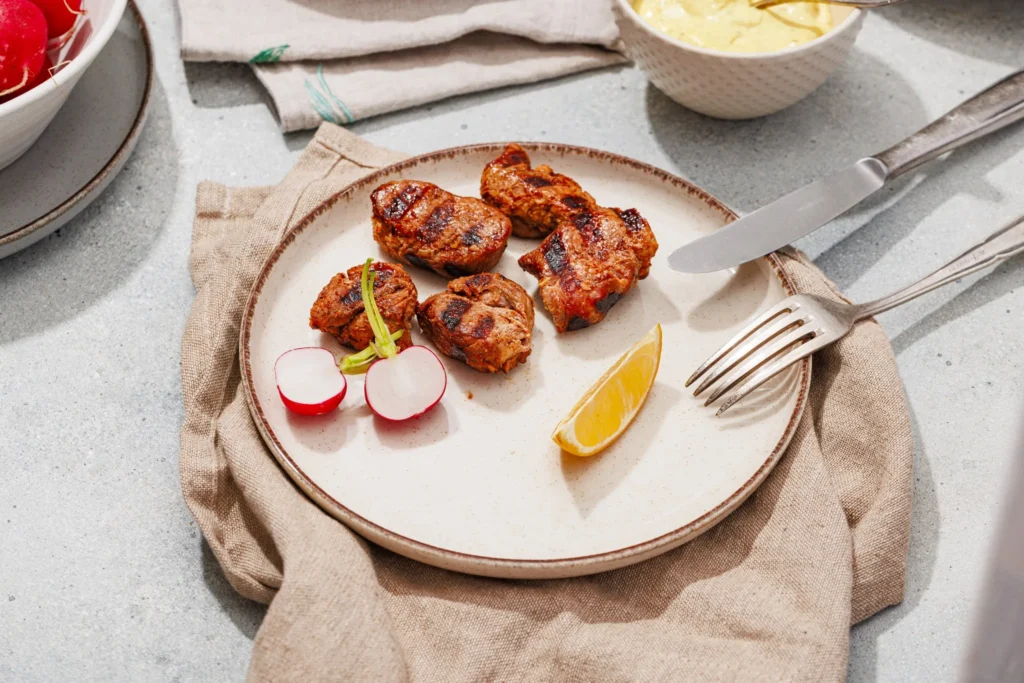 Grilled marinated pork pieces served with lemon wedges and fresh herbs.