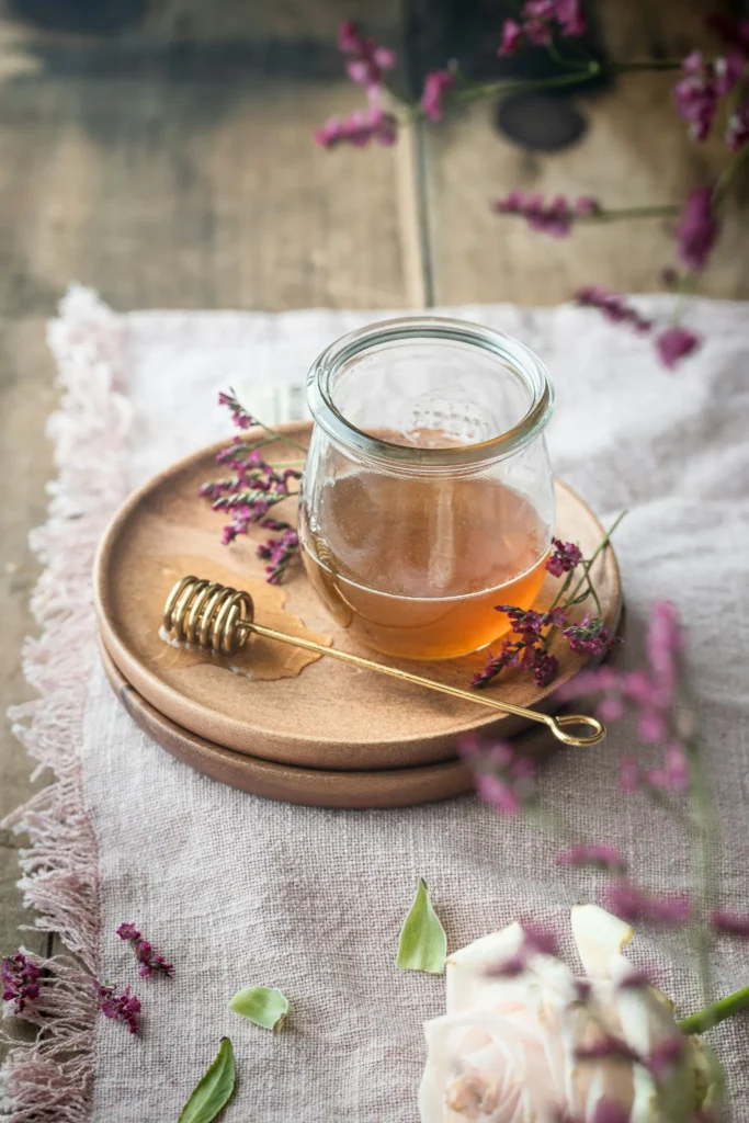 Glass jar of honey with a honey dipper and purple flowers