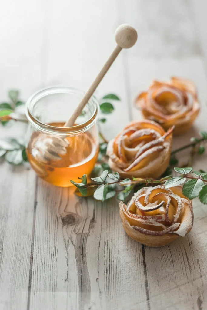 Glass jar of honey beside baked apple rose pastries