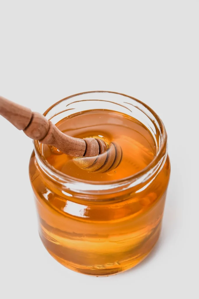 Glass jar of honey with a wooden honey dipper