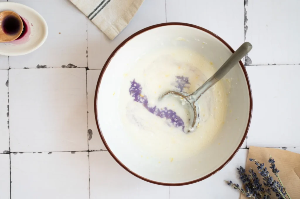 Lemon lavender glaze being mixed with lemon zest and purple coloring in a bowl.
