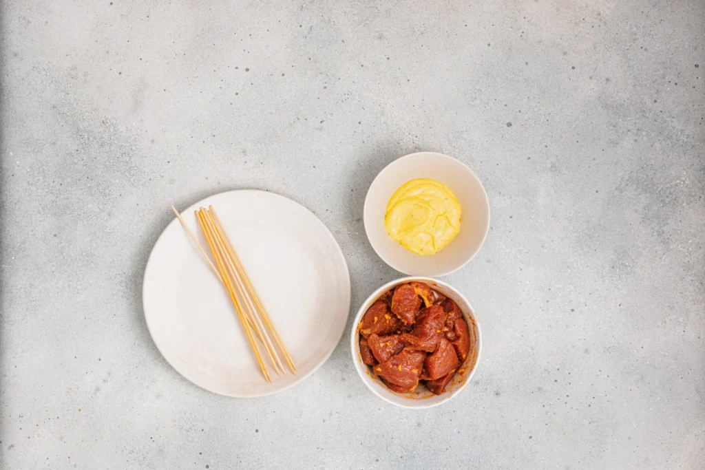 Marinated pork, wooden skewers, and homemade aioli ready for assembling pork skewers.