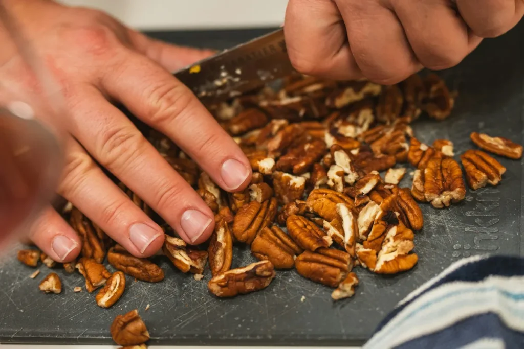 Chopping pecans with a kitchen knife on a cutting board