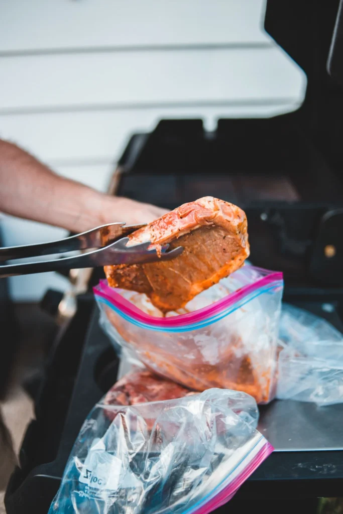 Marinated steak being removed from a resealable bag beside a grill