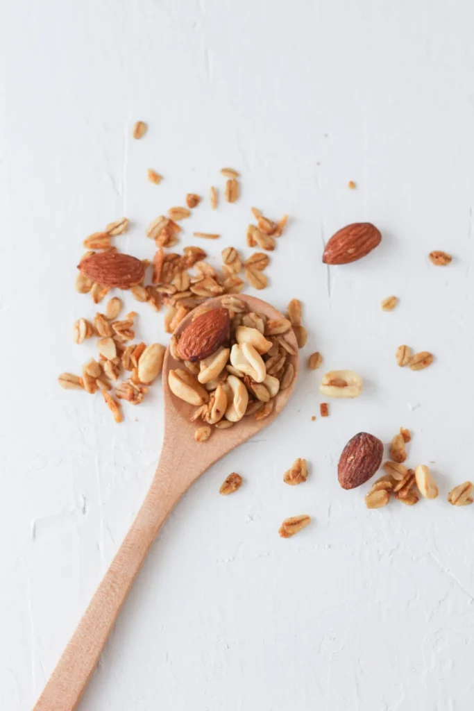 Almonds and peanuts mixed with granola on a wooden spoon