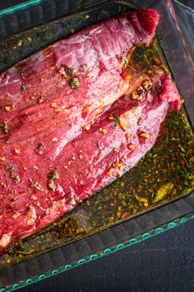 Raw steak in a garlic and herb marinade in a glass baking dish
