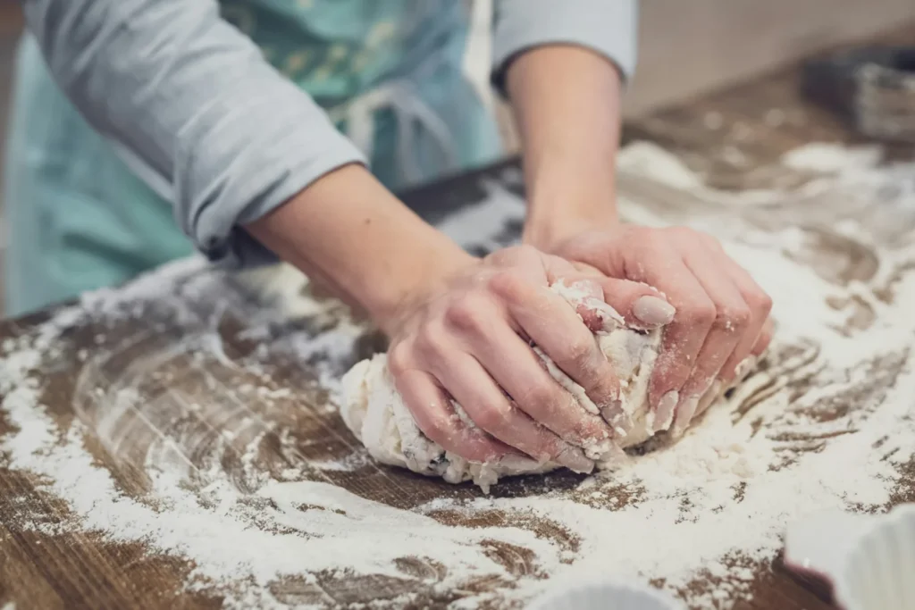 Hands kneading homemade bread dough on a lightly floured work surface.